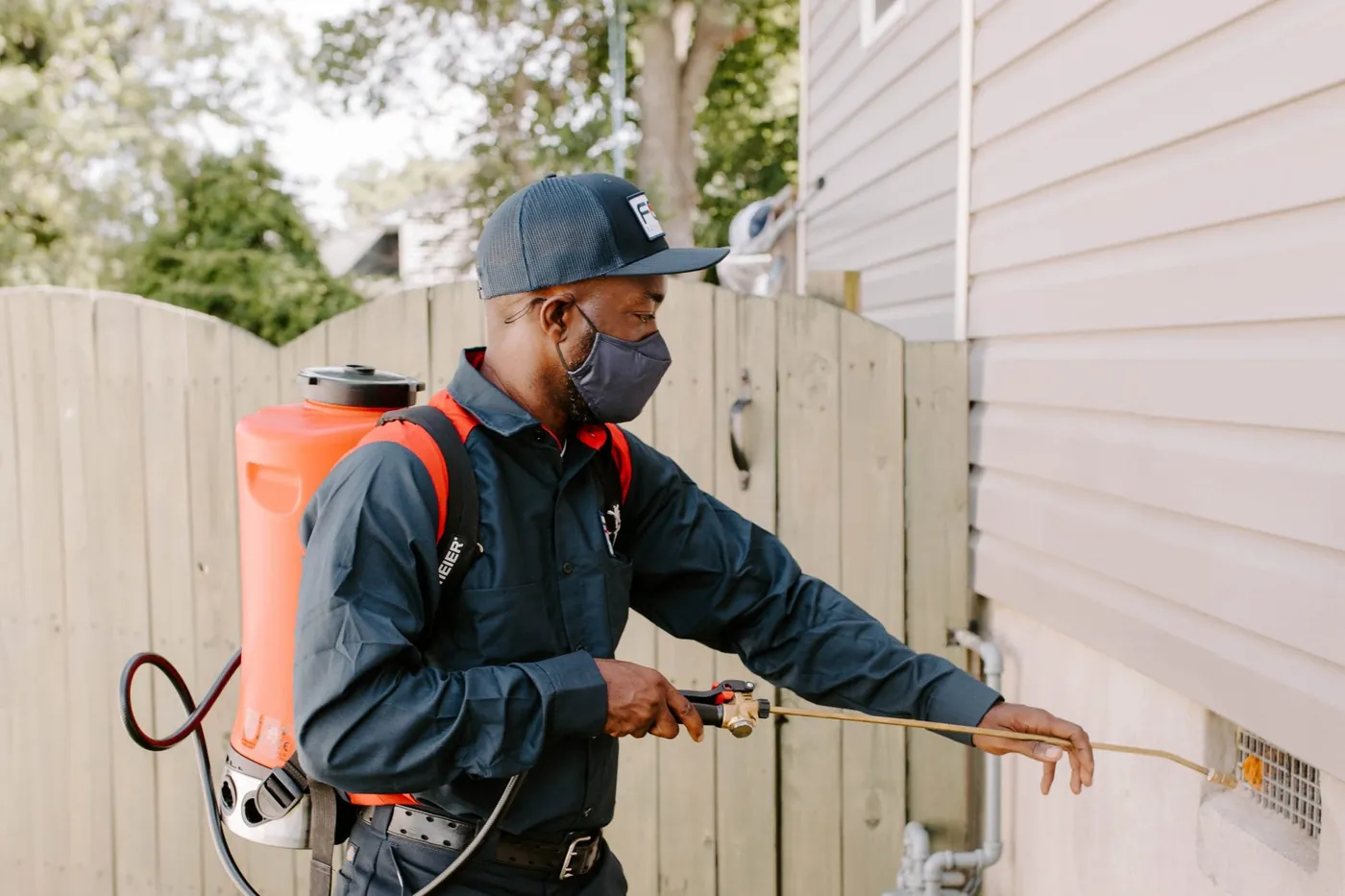 A pest control technician spraying treatment along the exterior foundation of a building in Alabama.